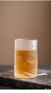 Close-up of frosted glass cup featuring 3D embossed cat patterns on vintage books