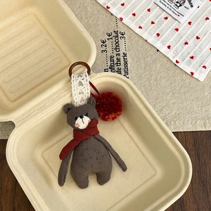 Detail of cute plush brown bear keychain with red knitted scarf and soft fuzzy pompom