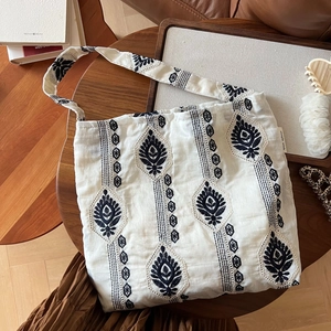 Détail de broderie bohème sur sac en coton beige posé sur une table en bois