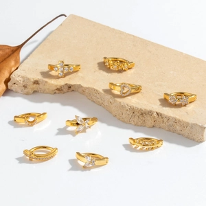 Golden belly rings with clear zircon pendants on a beige stone surface