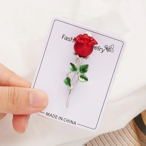 Detailed close-up of a red rose enamel brooch featuring green leaves and silver stem