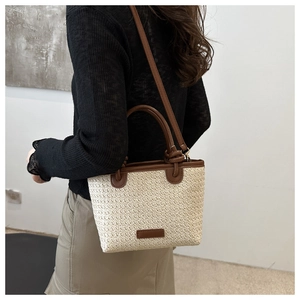 Detail of woven straw bucket bag with brown leather handles and textured ivory finish
