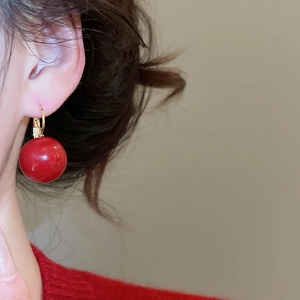 Detail of red resin bead earrings with gold plating on model for a festive look