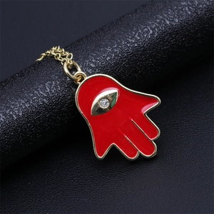 Macro view of gold Hamsa Hand pendant with red enamel and zircon on black display