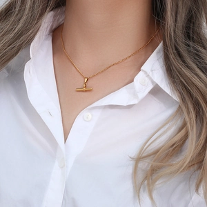Close-up of minimalist gold T-bar pendant necklace worn by a model in a white shirt