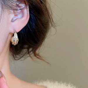 Close-up of elegant C-shaped gold earring with micro-set zircons and a white pearl