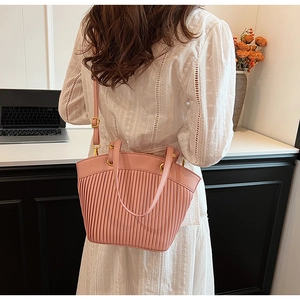 Pink pleated faux leather shoulder bag with gold metal rings shown on a woman's shoulder