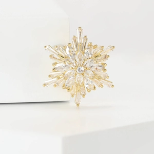 Elegant gold snowflake brooch with marquise crystals on a white geometric display