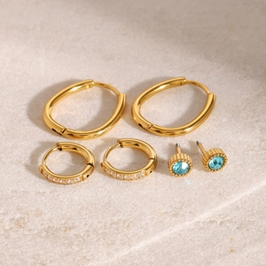 Three-pair set of gold stainless steel hoop earrings and zircon studs on marble