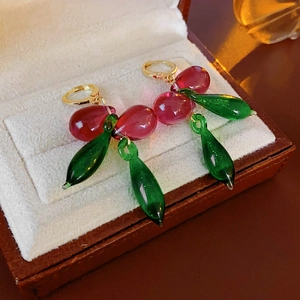 Détail de boucles d'oreilles en verre rouge et vert avec crochets dorés dans un écrin