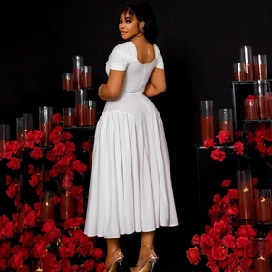 Elegant white pleated A-line dress with open back and waist detail in dark floral setting
