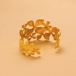 Macro view of a gold-colored stainless steel cuff with hollow floral pattern