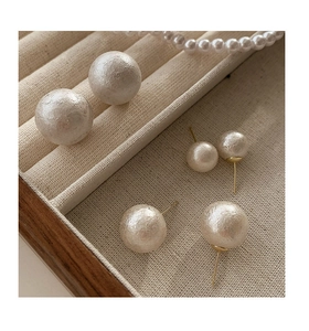 Macro shot of matte marshmallow pearl stud earrings with golden needles in two sizes