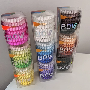 Close-up of stacked colorful spiral hair ties in transparent boxes with BOW lettering
