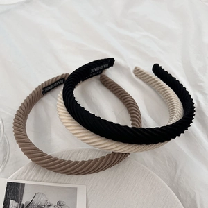 Three handmade ribbed headbands in brown, black and beige on soft white fabric background