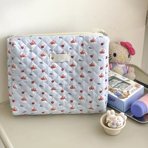 Detail of light blue quilted makeup bag with small red flowers and woven label