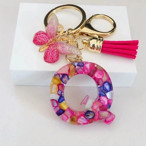Detail of resin letter Q keychain with pink butterfly and tassel on white base