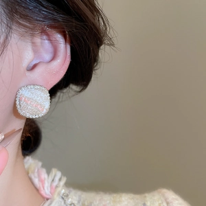 Detailed macro view of square tweed earrings with sparkling zircon borders worn by a model