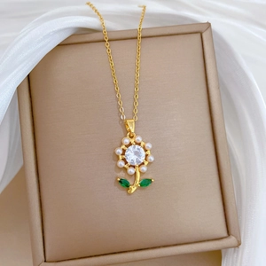 Close-up of gold sunflower necklace with a crystal core, pearls and green leaves