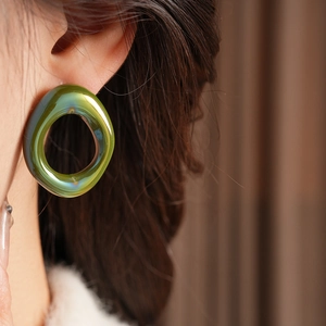 Close-up of model wearing green iridescent vintage glass hoop earrings with a glossy finish