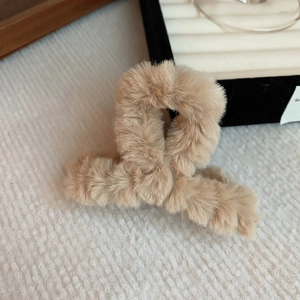 Close-up of beige plush faux fur hair claw clip with a twisted cross design on fabric