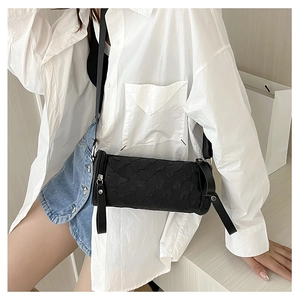 Close-up of black quilted cylindrical crossbody bag with wide shoulder strap texture