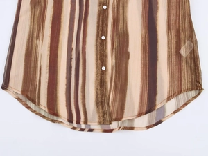Dettaglio dell'orlo curvo e dei bottoni bianchi sulla camicia a righe marroni e beige