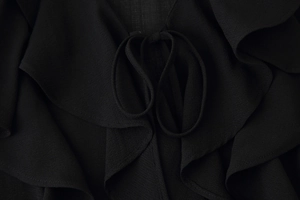 Detailed macro view of black chiffon fabric texture with ruffle edges and neckline ties