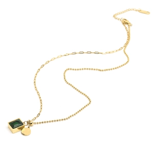 Detail of gold double-layer necklace featuring green square gemstone and round charm
