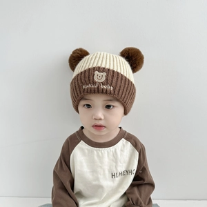 Detail einer Baby-Strickmütze mit Bären-Stickerei und doppelten Kunstpelz-Pompons