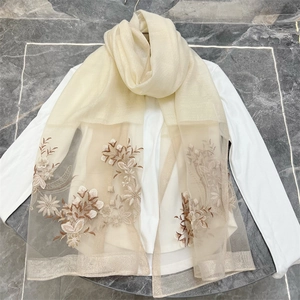Detailed embroidery of brown and beige floral patterns on a sheer beige mesh scarf texture