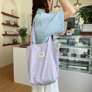 Detail of a purple plaid canvas tote bag with pink bow print on a model's shoulder