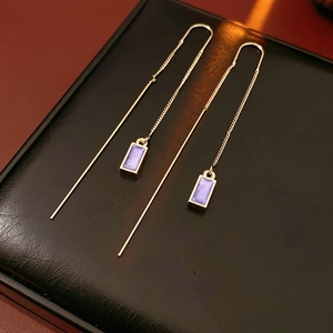 Macro shot of gold chain earrings with purple enamel rectangle charms on leather