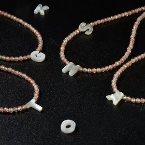 Detailed view of beaded necklaces with natural shell alphabet pendants on a dark surface