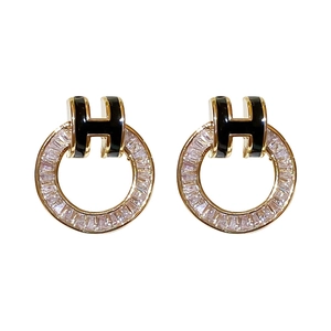Gold plated hoop earrings featuring sparkling zircons and a black enamel H-shaped charm