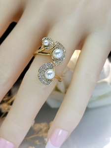 Close-up of golden lotus leaf ring with pearls and pavé diamonds on a finger