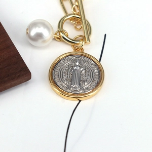 Close-up of Saint Benedict medal pendant with gold T-bar clasp and white pearl detail