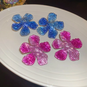 Close-up of floral cubic zirconia earrings in gradient blue and purple on a ceramic tray