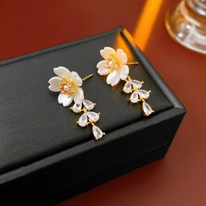 Detail of floral and teardrop earrings with crystals resting on a premium black gift box