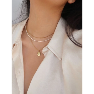 Detailed close-up of layered gold rose pendant necklace with white beads on model