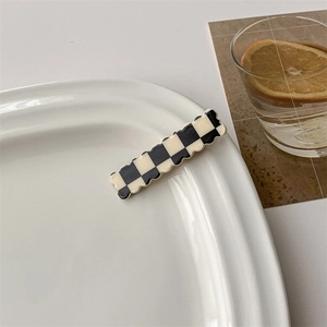 Detail of checkered hair clip with scalloped edges on a minimalist ceramic plate