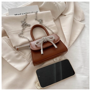 Detail of a brown mini handbag featuring a rhinestone bow and silver chain strap
