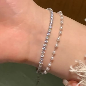 Close-up of stacked silver bracelets featuring sparkling cubic zirconia and small round pearls