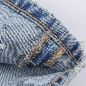 Détail du denim bleu clair avec des bords effilochés et des doubles coutures orange