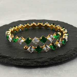 Elegant gold spiral bracelet with green and white cubic zirconia on a dark stone base