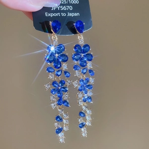 Close-up of dangling blue floral earrings with sparkling crystals and silver posts