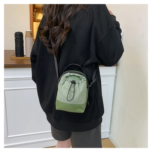 Olive green nylon drawstring crossbody bag shown as a compact bucket style on model