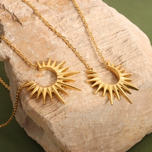 Golden geometric sunburst pendant necklaces on stone background with thin cross chains