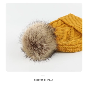 Detail of a ginger yellow winter knit beanie with a fluffy brown faux fur pom pom