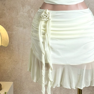 Detail of cream high-waisted mini skirt featuring 3D rose decor and ruffled hemline